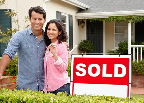 A couple standing in front of their home with the sold sign.