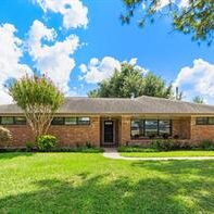 A large brick house with grass and trees in front of it.